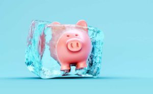 Piggy bank frozen in ice cube on blue background